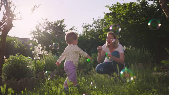 Summertime. Smiling young mother blows soap bubbles. Little baby playing with bubbles. Slow motion.