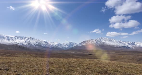 Timelapse of Sun Movement on Crystal Clear Sky with Clouds Over Snow Mountain Top. Yellow Grass at