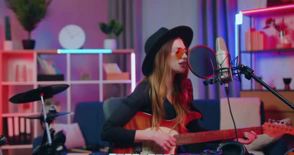 Woman with Long Hair Wears Hat and Sunglasses Sitting in front of Recording Equippment in home