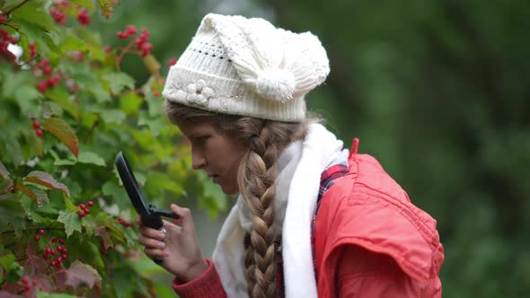 Side View Focused Teenage Girl Examining Viburnum with Magnifying Glass Outdoors