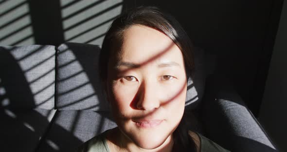 Thoughtful asian woman sitting on sofa close to window at home