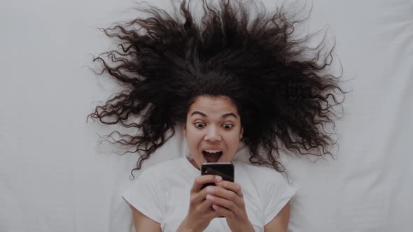 African American Female Pleasantly Surprised Looking at the Smartphone Delighted with Notifications
