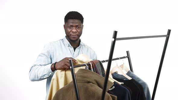 Proud Elegant Black Man Wearing a Denim Shirt Picking an Outfit From a Self Standing Clothes Rack