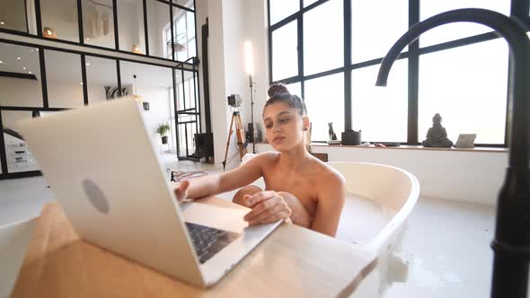 Young Woman Working on Laptop While Taking a Bathtub