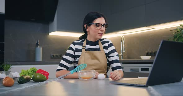 Girl Sitting in front of Laptop and Talking with Female Friend Explaining Her How to Prepare Egg