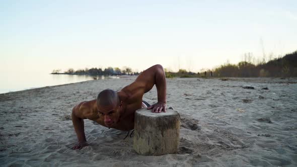 Muscular athlete doing push-ups on a beach in slow motion