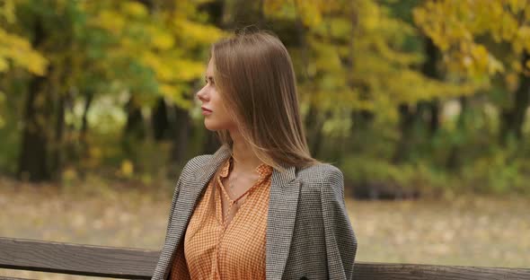 Profile Portrait of an Elegant Caucasian Woman Sitting on the Bench in the Park and Smiling