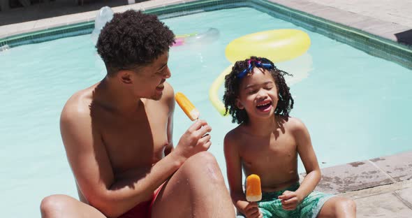 Happy biracial man and his son eating ice cream by swimming pool in garden