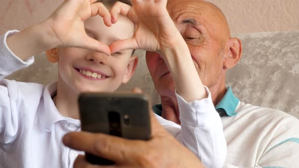 happy caucasian grandfather 70 years old and grandson 7 years old take a selfie on the phone at home