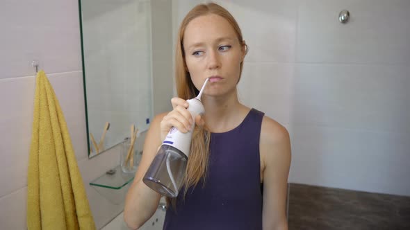 A Young Woman Uses a Portable Water Flosser Dental Oral Irrigator To Clean Her Teeth. Teeth Care