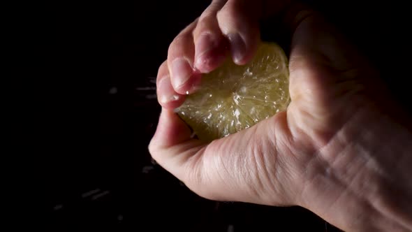 Male hand Squeeze Lime, Lemon Juice dropping on transparent surface.Slow motion shot with black back