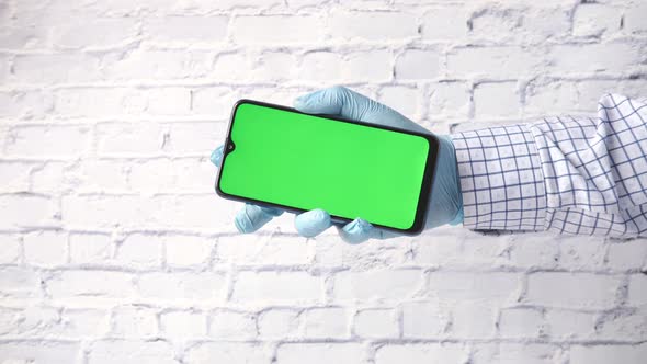 Hand in Latex Gloves Holding Smart Phone with Green Screen
