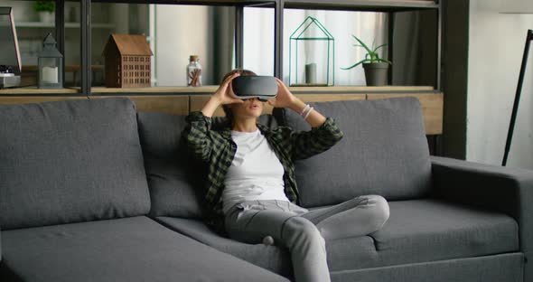 Young Woman Is Putting Virtual Reality Headset On, Relaxing on Sofa