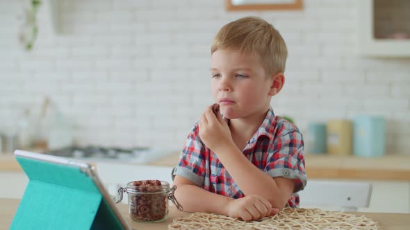 Young boy eating corn flakes and watching tablet computer at home