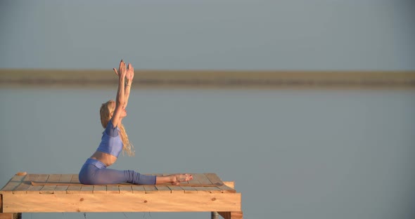 Yoga Outdoors By a Blonde Young Woman on a Wooden Platform in the Lake
