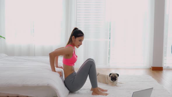 Asian woman in sportswear workout excercise online course at home with dog