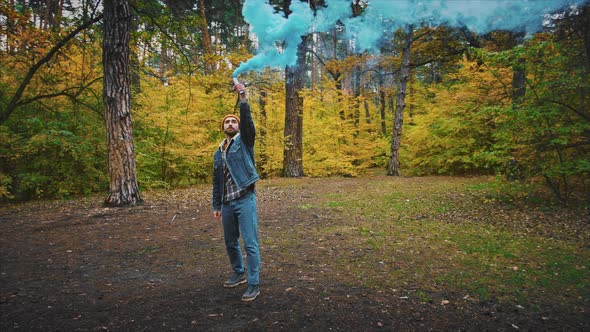 Young Man in Forest Having Fun with Blue Smoke Grenade in Autumn Forest 360 Degree Tracking Arc Shot