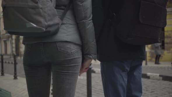 Young Caucasian Man and Woman Taking Each Other's Hands and Walking Away Along Town Street