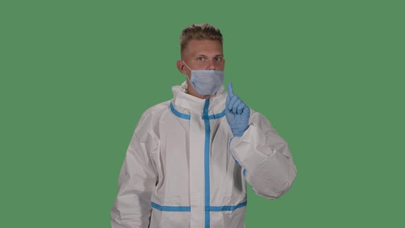 Portrait of a Man in a Protective Suit and Medical Mask Looks Into the Camera and Shows How To