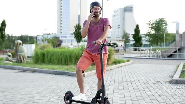 A Man in a Park on an Electric Scooter Talks on the Phone and Laughs