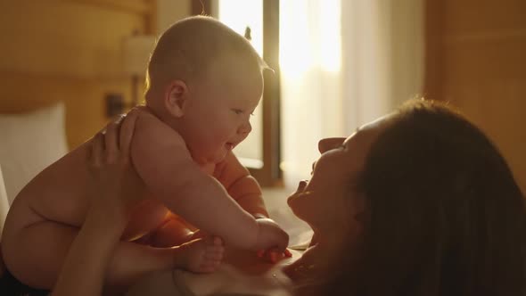 Asian Woman Mother Holding Baby Infant in Arm Playing and Talking with Kid on Sofa Couch in Living