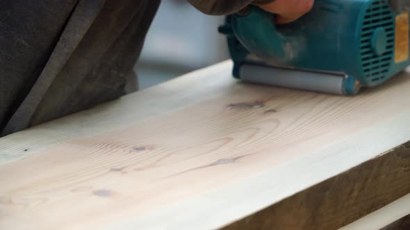 Working Man Is Polishing a Piece of Wood with a Machine for Grinding in the Hands