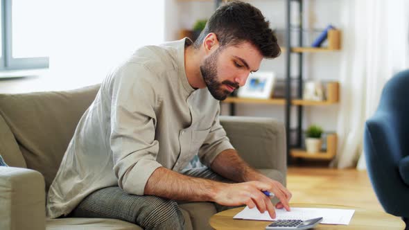 Man with Bills Counting on Calculator at Home