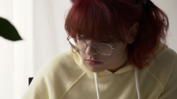 Closeup view on young redhead Ukrainian teen girl sitting at a table with notebooks, preparing for a