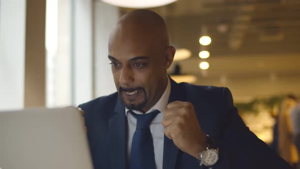 Happy African American Businessman Looking at Laptop Raising Fists Sitting in Cafe