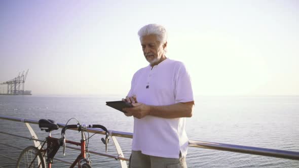 Portrait of Retirement Handsome Senior Man Using Tablet Computer on Seafront Slow Motion