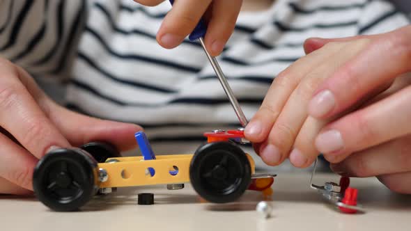 Close-up of the Hands of a Child and a Woman. Mother and Son Play By Assembling a Car Model From a