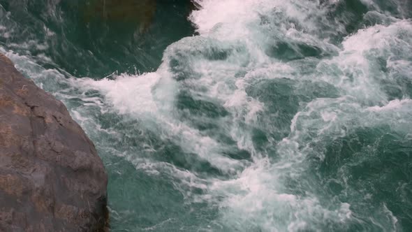 Close up of clear blue water raging down a river full of rocks in the France countryside.