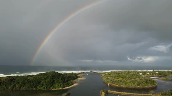 Large colorful rainbow located on a scenic coastal river inlet near a popular holiday spot. High pan