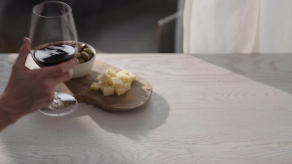 Man Hand Take Red Wine in Wineglass with Antipasti on White Oak Table