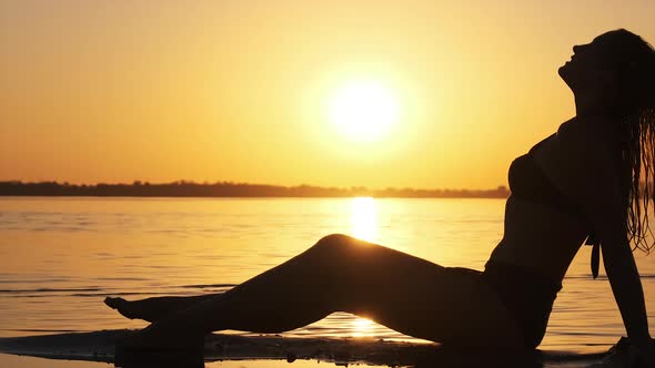 Silhouette of Hot Woman in Swimsuit Lying and Posing on Evening Beach at Sunset