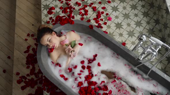 Sexy Girl Lies in a Big Stone Bath with a Rose Flower in Her Hands