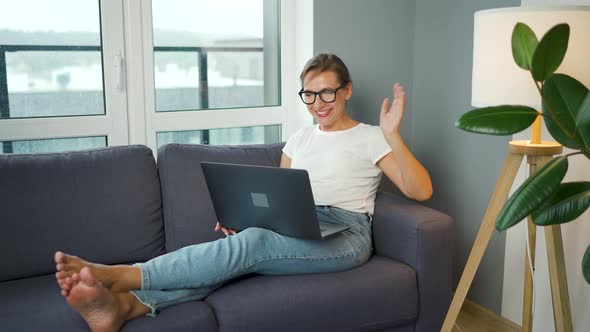 Casual Dressed Woman with Glasses Sitting on the Sofa and Communicates Via Video Link with Family or