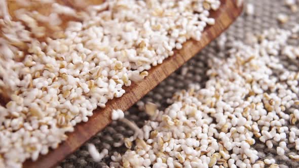 Popped amaranth grains. Falling on a rustic burlap surface and wooden kitchenware