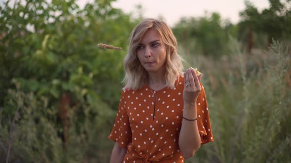 Attractive Fun Hippie Blonde Woman Eating an Apple in a Field at Sunset Having Good Time Outdoors