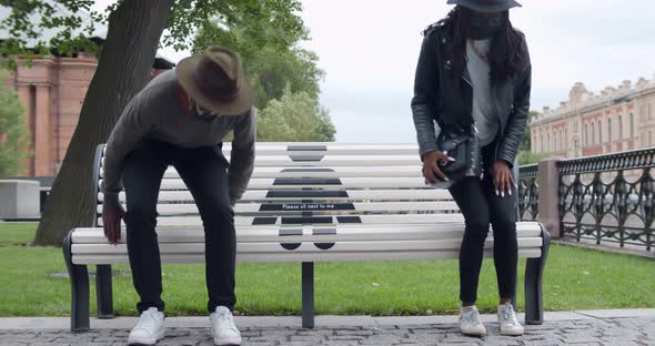 African Young Man and Woman in Safety Mask Sitting on Bench in Park During Coronavirus Outbreak