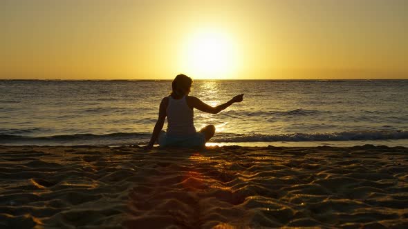 Silhouette of Woman Sitting on Golden Sand at Sunset Sand Through Fingers