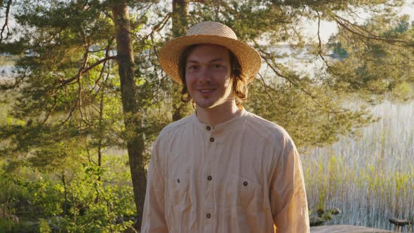 Young Man in Straw Hat Smiles Looking Straight on River Bank