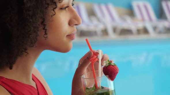 Portrait of Curly Afro Woman in Red Swimsuit Sitting Poolside Enjoying Drinking Cool Fruit Cocktail