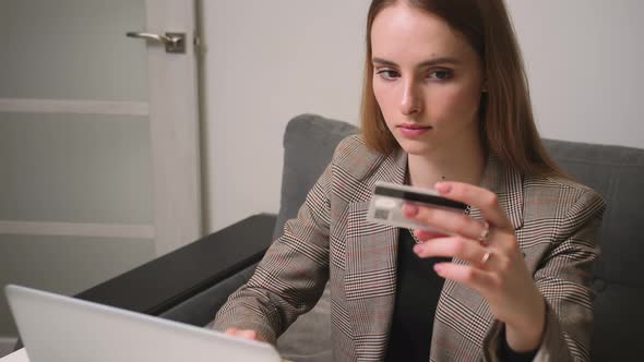 Pretty Young Woman Making Online Payment Holding Bank Card Using Laptop at Home