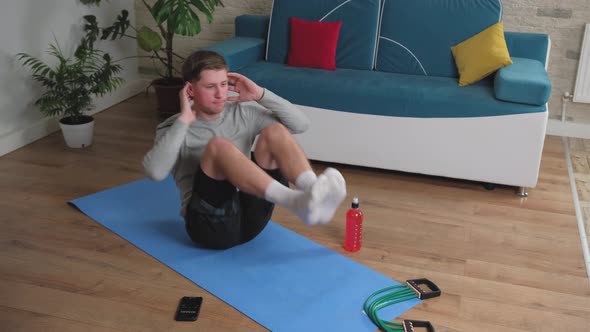 Young Man Doing Abdominal Exercises at Home on a Blue Mat