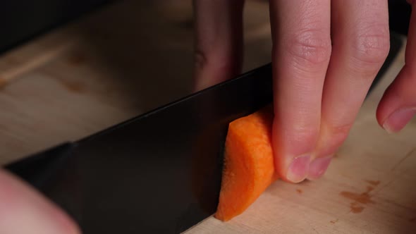 Chef hands cuts carrots pieces in half on wood chopping board.