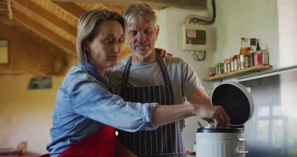 Smiling senior caucasian couple wearing aprons, composting vegetable cuttings in kitchen