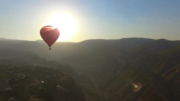 Aerial View of Hot Air Balloon Flying Over Mountain Village at Beautiful Sunset