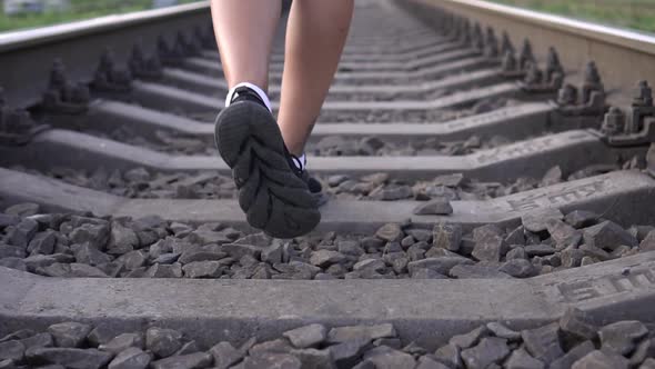 A Woman Walks Along the Sleepers on the Railroad Legs in a Closeup Shot in Slow Motion