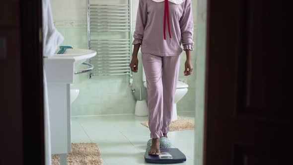 Pedestal Shot of Slim Young African American Woman Stepping on Bathroom Scales in Slow Motion